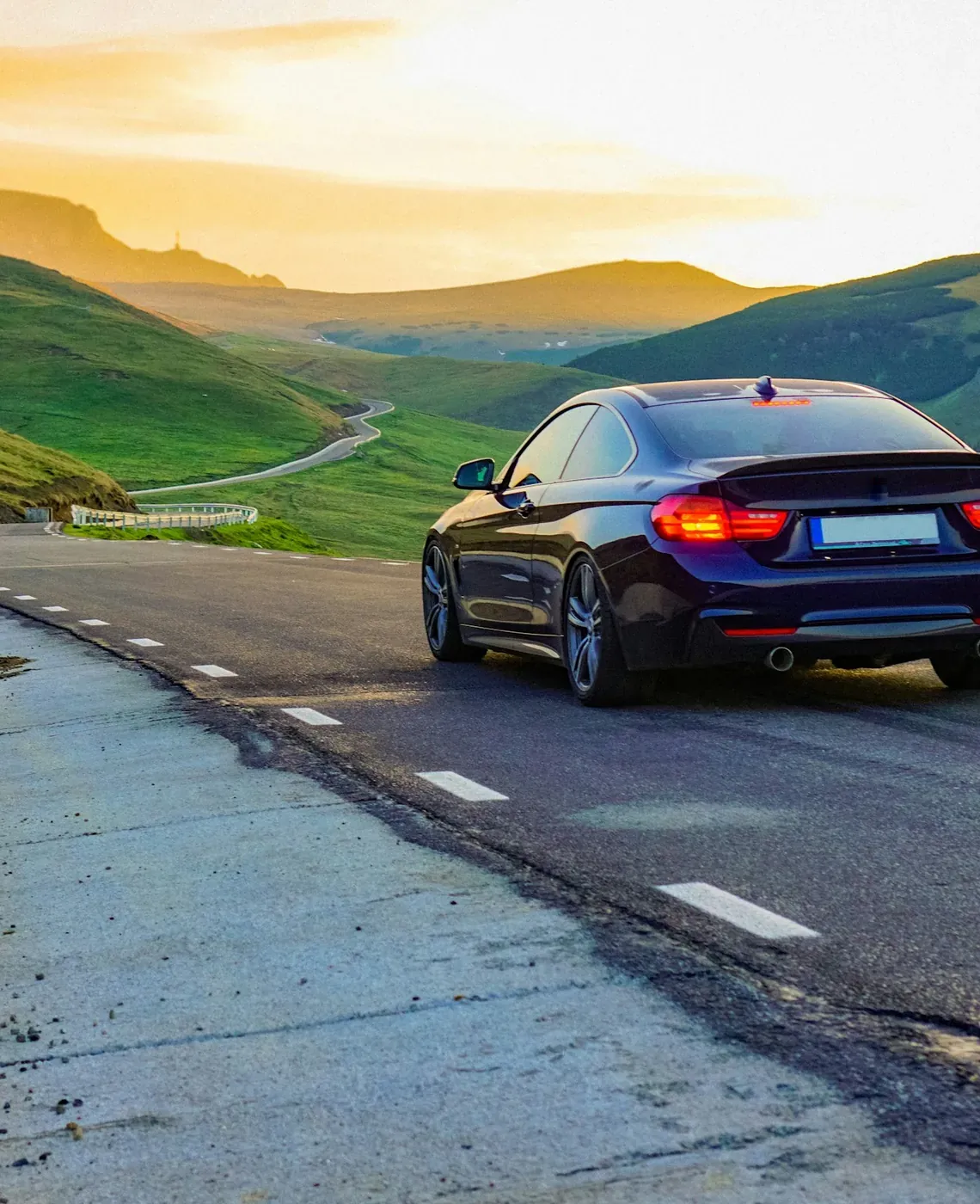 Dark sedan driving a winding mountain road at sunset