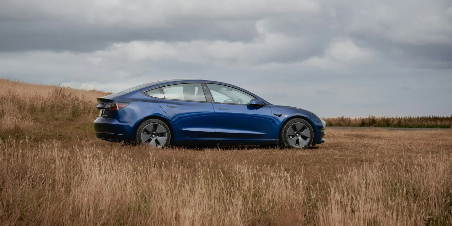 Blue electric sedan parked in a field of tall grass
