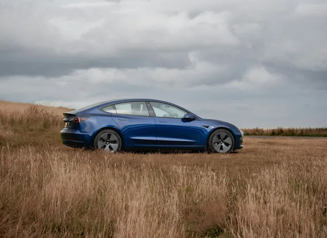 Blue electric sedan parked in a field of tall grass